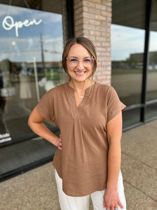 Woman smiling outside boutique wearing a relaxed short-sleeve V-neck blouse with white pants.