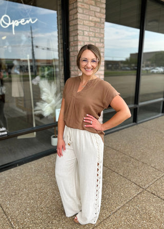 Woman wearing a casual short-sleeve V-neck blouse paired with white linen wide-leg pants outdoors.