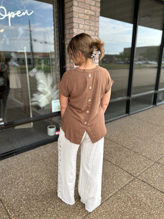 Woman wearing a short-sleeve button-back blouse with split hem, paired with wide-leg pants.