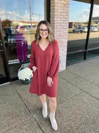 Woman wearing a v-neck balloon sleeve mini dress with pockets, paired with ankle boots.