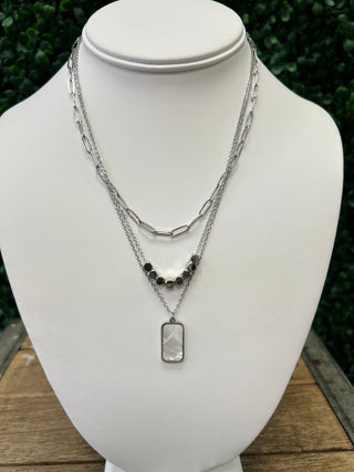 Layered silver chain necklaces with dark beads and rectangular pendant displayed on white jewelry bust
