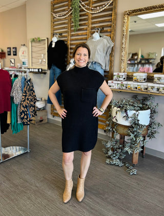 Woman wearing black ribbed sweater dress standing in boutique store with hands on hips