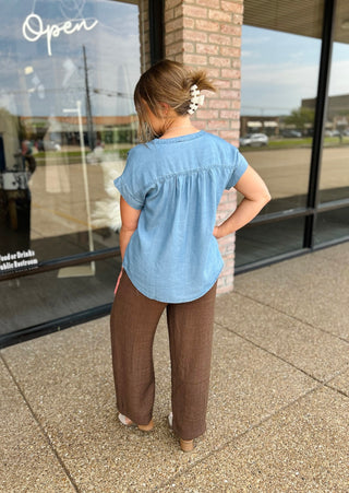 Woman seen from behind wearing a Classic Chambray Henley Blouse paired with wide-leg trousers.