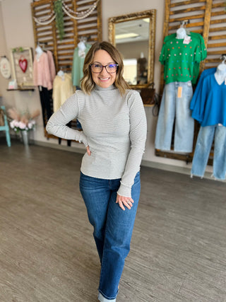 Woman wearing striped mock neck top and jeans standing in clothing boutique