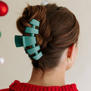 Woman wearing large teal hair clip in twisted updo hairstyle with gold hoop earring.