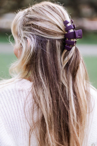 Woman wearing a purple hair clip in blonde wavy hair styled in half-up ponytail