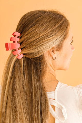 Woman wearing coral-colored medium hair clip in blonde hair against peach background