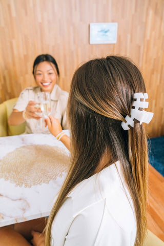 Woman wearing white TELETIES hair clip in long brown hair while relaxing with friend