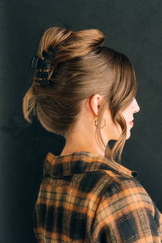 Woman wearing a black hair clip in an updo hairstyle with plaid shirt, profile view.