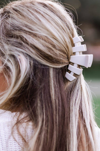 Woman wearing beige hair clip in blonde highlighted hair styled in half-up ponytail.