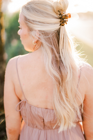 Woman with blonde wavy hair wearing a tortoise hair clip in a half-up hairstyle outdoors.