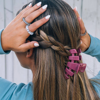 Woman with braided hair wearing pink hair clips and white manicured nails touching her hairstyle.