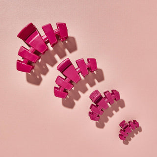 Pink hair clips scattered on textured pink surface casting shadows in bright lighting