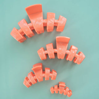 Four coral-colored curved hair clips arranged on a mint green background