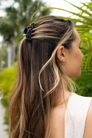 Woman wearing black hair clip in brown highlighted hair with tropical plants in background