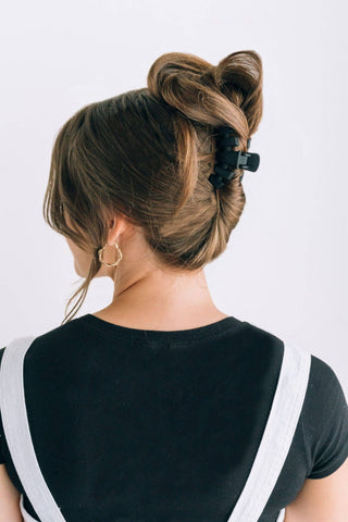Woman wearing a messy bun hairstyle secured with a small dark hair clip, viewed from behind.