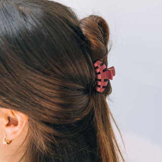 Woman with brown hair wearing a coral pink claw clip hair accessory in a half-up hairstyle.