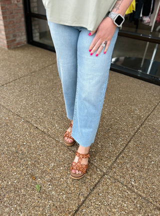 Woman wearing light wash cropped straight leg jeans with brown sandals and pink nail polish
