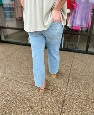 Person wearing light blue cropped straight leg jeans with cream top and woven sandals walking outdoors