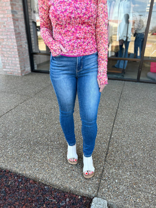 Woman wearing classic tummy control skinny jeans with pink floral top and white sandals outdoors.