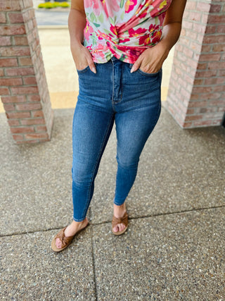 Woman wearing classic tummy control skinny jeans with floral top and brown sandals on concrete sidewalk.