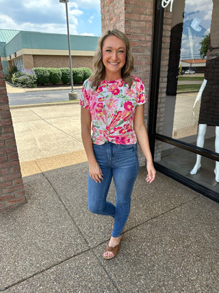 Woman wearing floral pink top and blue skinny jeans standing outside boutique storefront