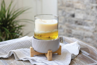 Classic wooden pedestal candle warmer with lit candle in glass holder on striped fabric