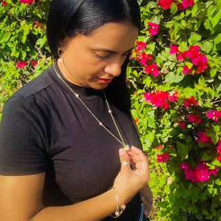 Woman wearing gold conch shell necklace outdoors with vibrant flowering plants in background