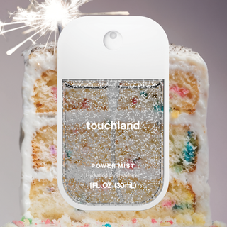 Touchland Power Mist hand sanitizer with glitter bottle in front of a festive layered cake with sparkler.