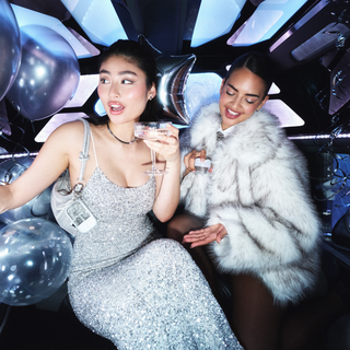 Two stylish women celebrating in a limo holding Touchland Confetti Cake Power Mist Hand Sanitizer.