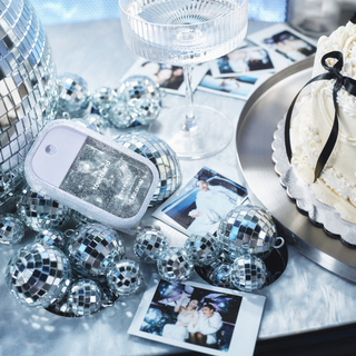 Touchland Power Mist hand sanitizer surrounded by mini disco balls, Polaroid photos, champagne coupe, and white cake.