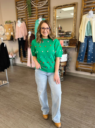 Woman wearing light wash barrel jeans with green polka dot sweater in clothing boutique setting