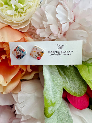 Colorful floral confetti square stud earrings on white card surrounded by fabric flowers