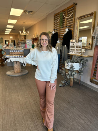 Woman wearing white sweater and copper-colored flare pants standing in retail boutique store
