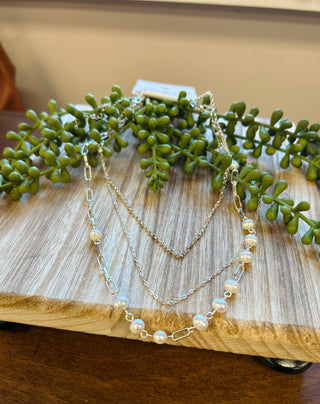Delicate layered silver chain necklace with pearls displayed on wooden surface with green succulent plants