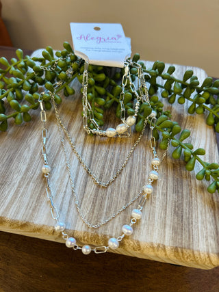 Layered silver chain necklace with pearl beads displayed on wooden surface with green succulent plant