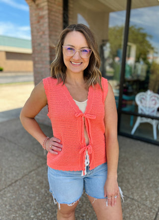 Woman wearing coral knit tie-front cardigan vest with denim shorts, smiling outdoors