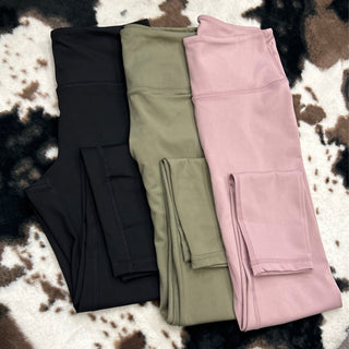 Three pairs of high-waisted compression leggings with side pockets in different colors displayed on cowhide rug.