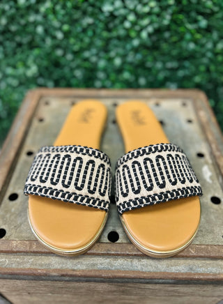 Corky's black and white patterned slip-on sandals with tan soles on wooden surface