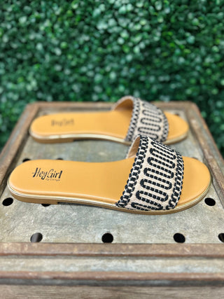 Corky's slide sandals with black and white patterned straps and tan footbeds on wooden surface.