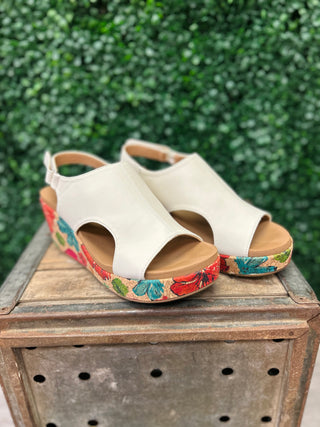 White wedge sandals with colorful floral platform soles displayed on rustic wooden crate outdoors.