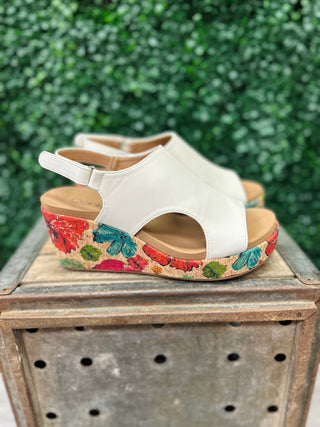 White wedge sandals with colorful floral cork platform sitting on wooden crate outdoors