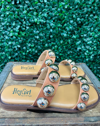Corky's studded slide sandals with metallic dome embellishments on cognac straps displayed on wooden surface