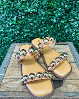 Corky's Catch A Buzz cognac sandals with metallic studs on wooden surface with green foliage background