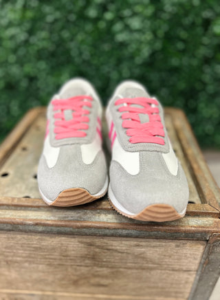 Grey and pink athletic sneakers with white accents displayed on wooden surface outdoors