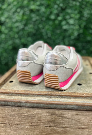 Grey sneakers with pink accents and brown soles displayed on wooden surface outdoors.