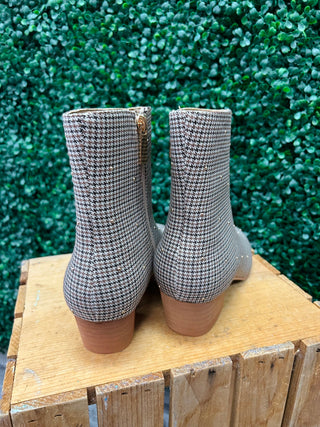 Corky's houndstooth patterned ankle boots with block heels displayed on wooden crate against green foliage background