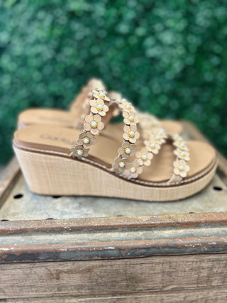 Corky's wedge sandals with floral embellishments and pearls on wooden surface with green foliage background