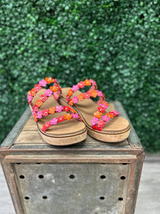 Colorful flower-adorned wedge sandals with cork platform soles displayed on wooden surface outdoors.