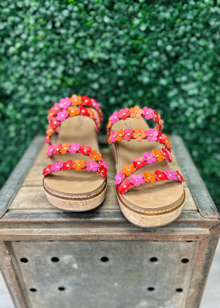 Colorful floral wedge sandals with multiple straps displayed on wooden crate outdoors